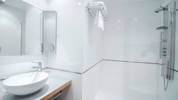 Un baño moderno con ducha envuelta en vidrio, un lavabo blanco y un perchero para toallas.