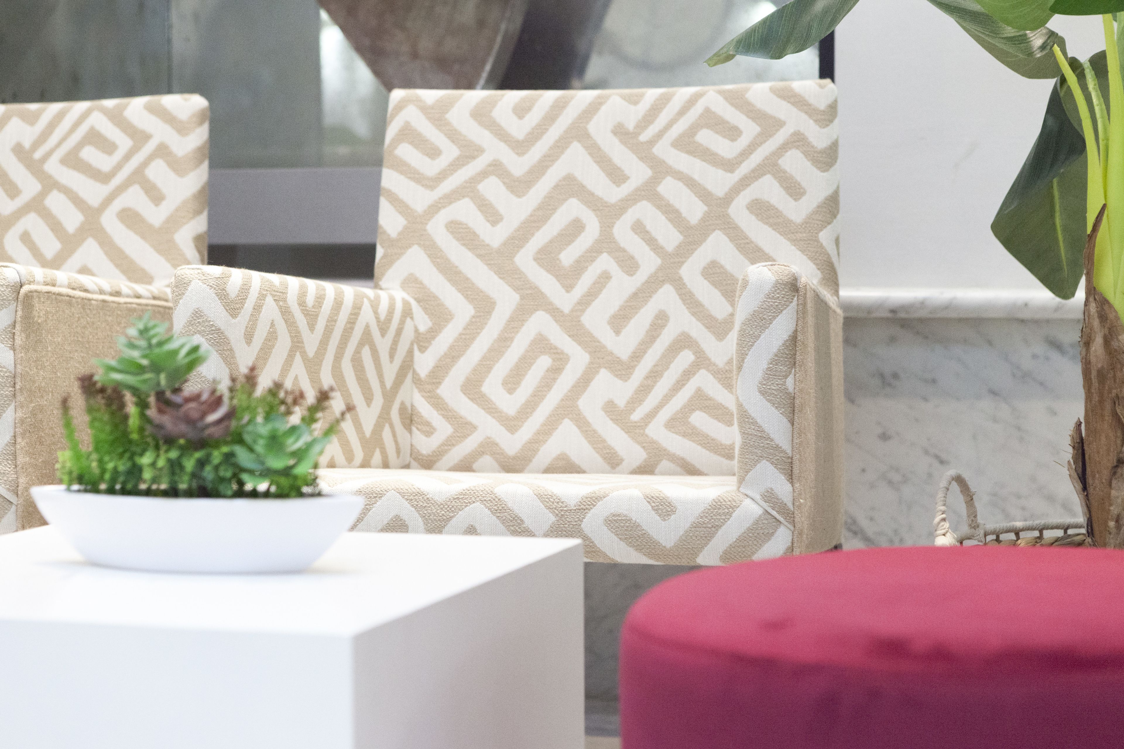 Una sala de estar moderna con sofás estampados, una mesita auxiliar blanca y un otoman rojo.
