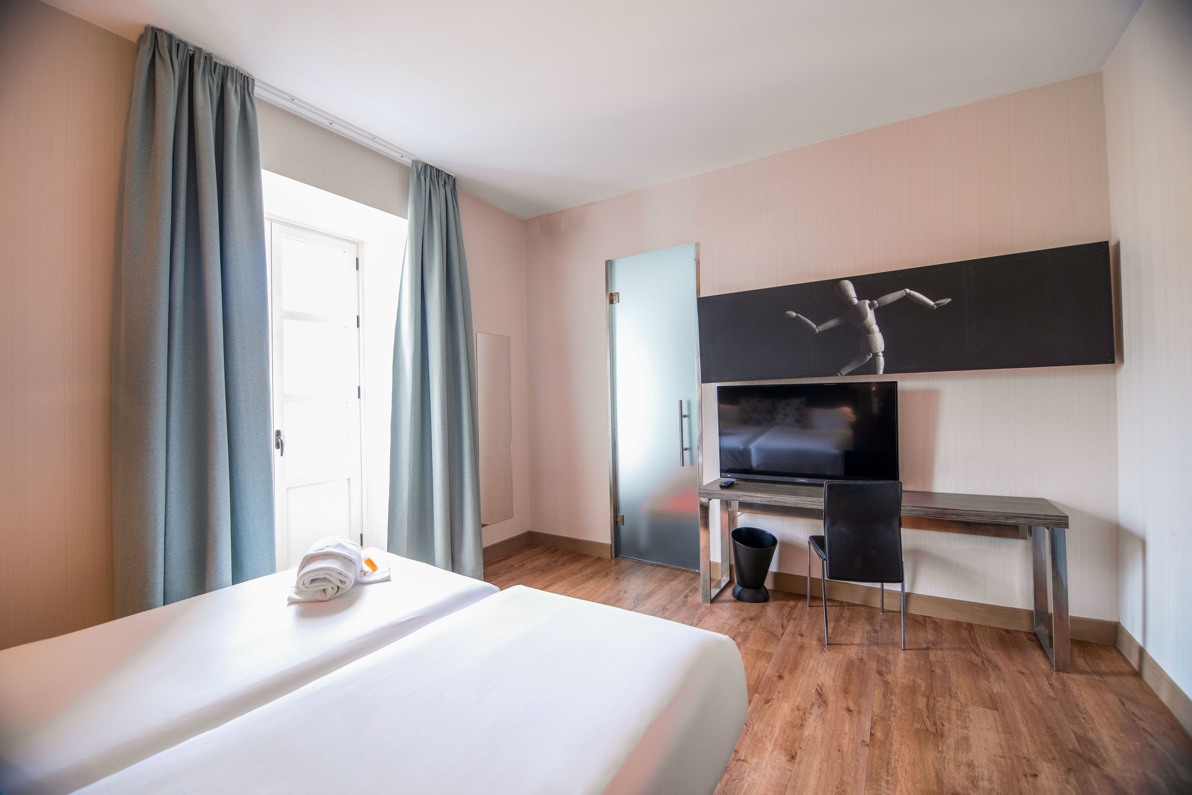 Una habitación de hotel con una cama, un escritorio, una silla, un televisor y una puerta.