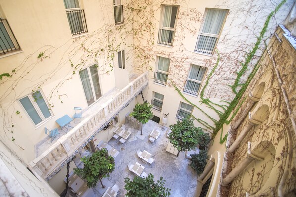 A courtyard with outdoor seating, trees, and a view of the surrounding buildings. - Petit Palace Santa Cruz (Seville)