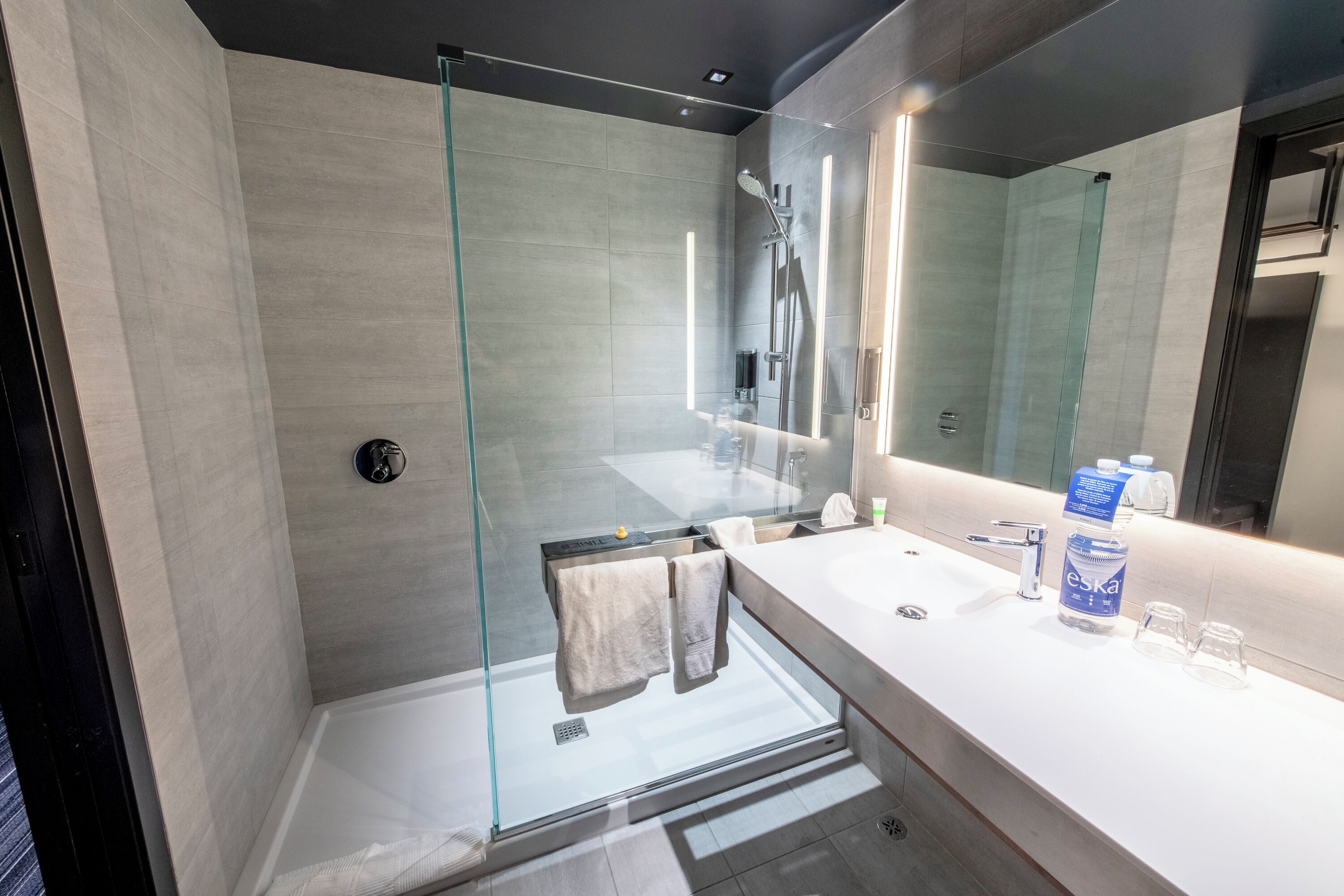 Un baño moderno con cabina de ducha de vidrio, un lavabo blanco y un espejo grande.