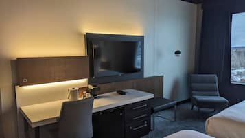 A modern hotel room with a flat-screen TV mounted on the wall, a desk with a chair, a bench, and a bed.