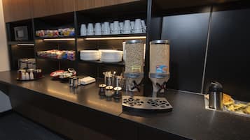 Zona de buffet amb diversos aliments, com ara cereals, condiments i una màquina de cafè.
