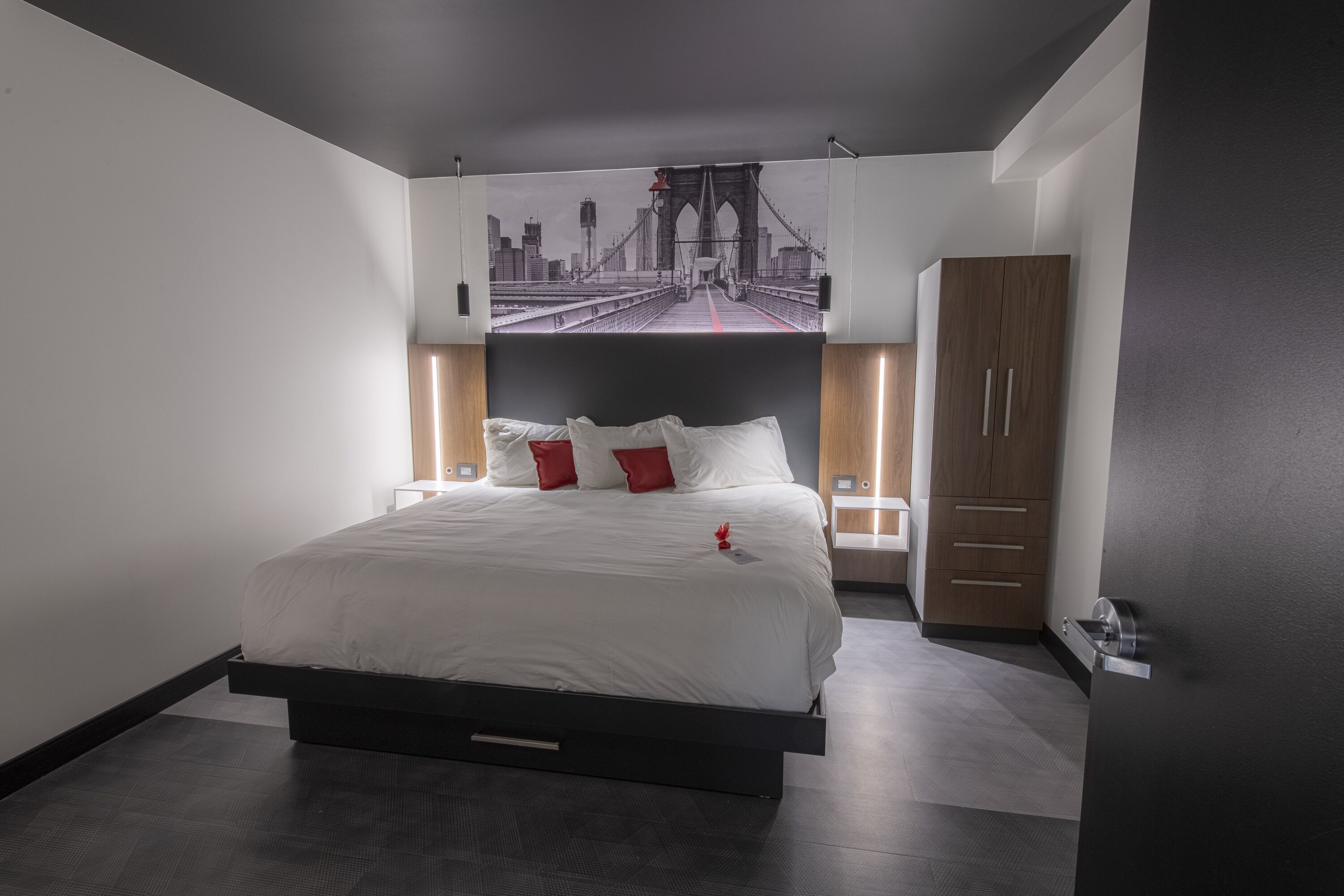 A modern bedroom with a large bed, a cityscape mural on the wall, and a wooden wardrobe.