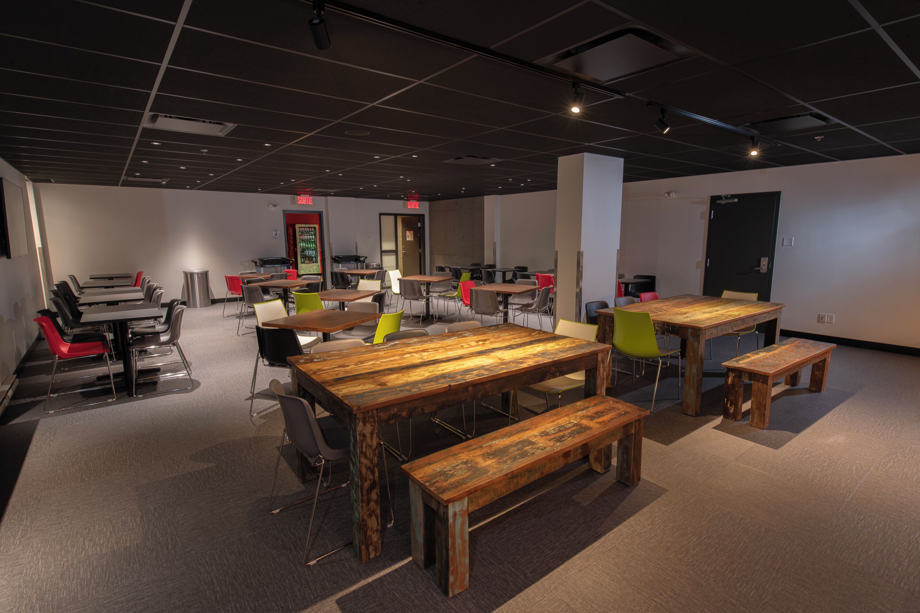 Une salle de conférence moderne, dotée de plusieurs tables et chaises, d’un espace pour préparer le café et d’un distributeur automatique.
