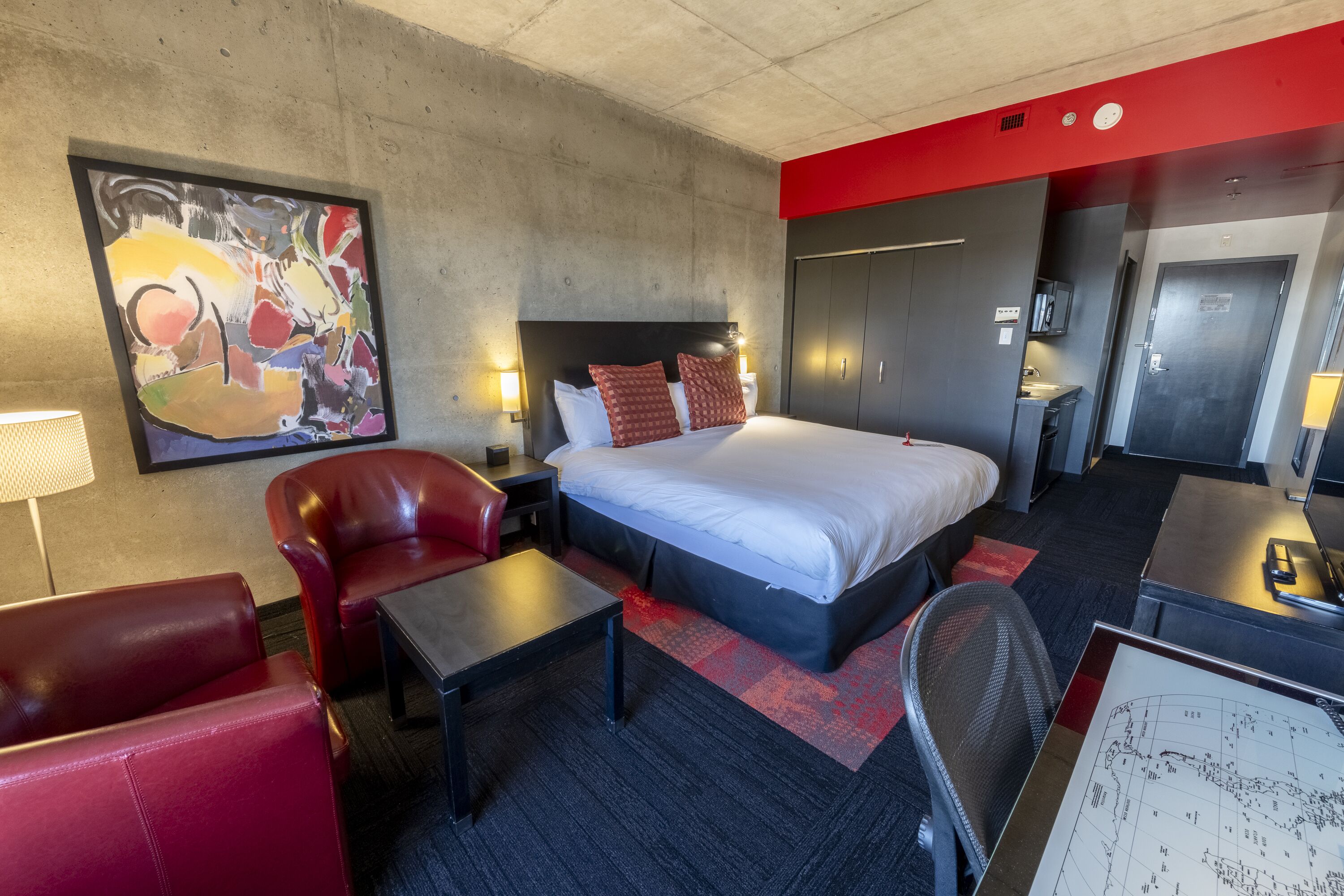 Una camera d'albergo con un letto grande, una scrivania, una sedia, un divano rosso, una mappa sulla scrivania e un quadro al muro.