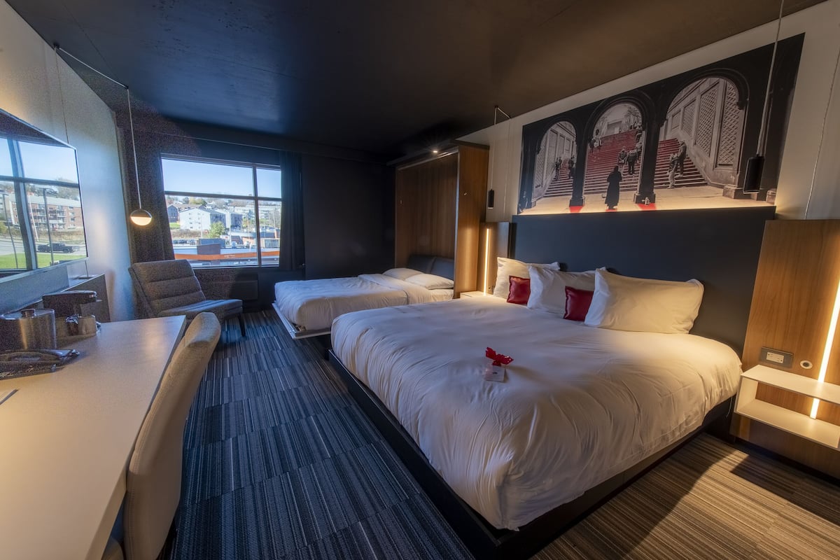 Habitación de hotel con dos camas, un escritorio y un ventanal grande.