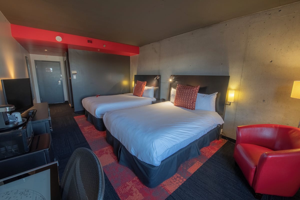 Habitación de hotel con dos camas, un escritorio con computadora, una silla roja y una alfombra roja.