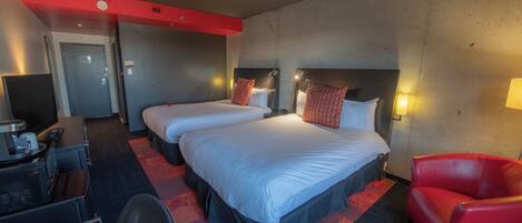Habitación de hotel con dos camas, un escritorio con computadora, una silla roja y una alfombra roja.