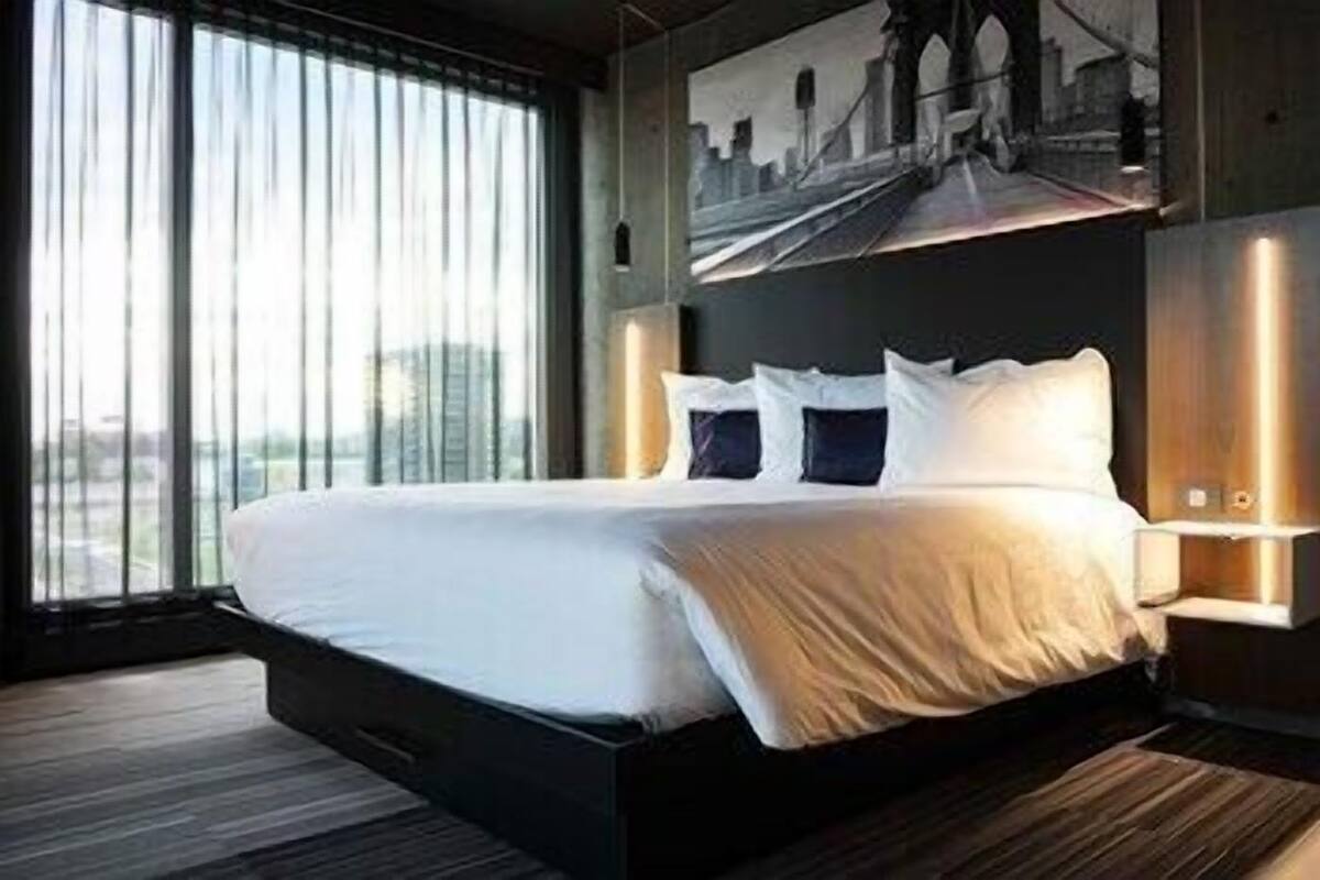 Una habitación de hotel moderna con una cama grande, vistas a un paisaje urbano y un diseño arquitectónico distintivo.