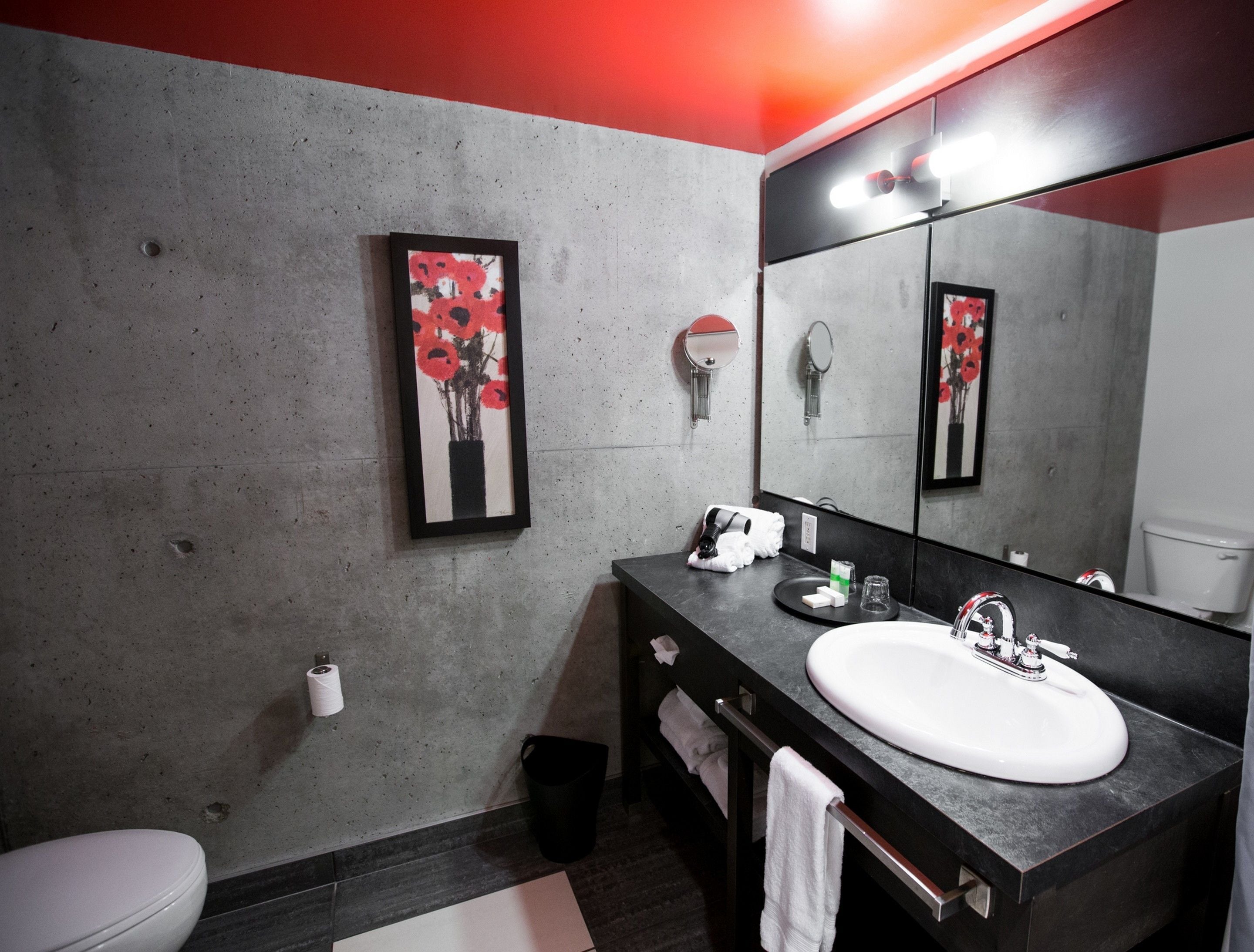 Un baño moderno con un espejo grande, un lavamanos blanco y una obra de arte floral enmarcada en la pared.