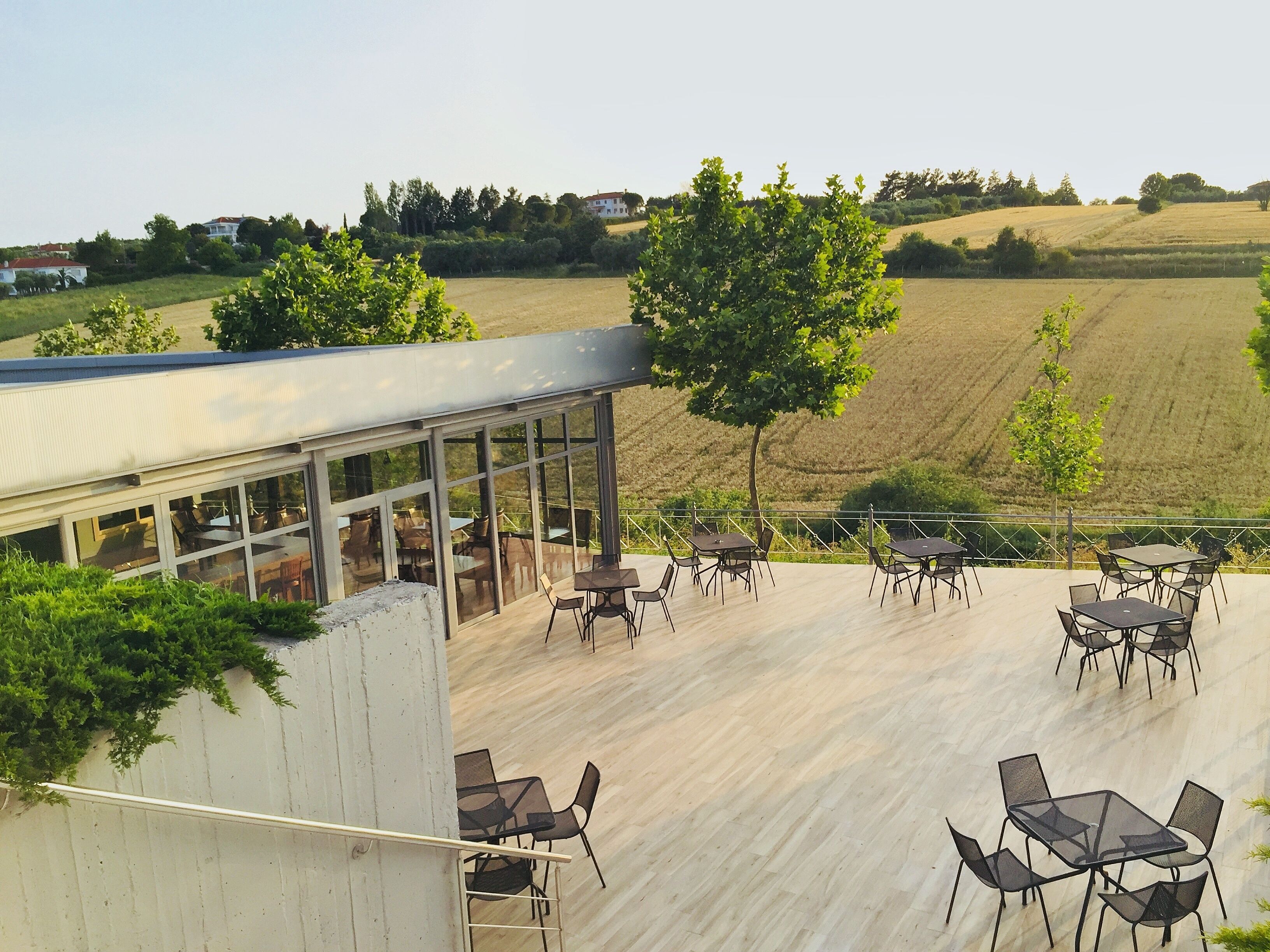 An outdoor patio with tables and chairs, overlooking a hilly landscape with fields and trees.