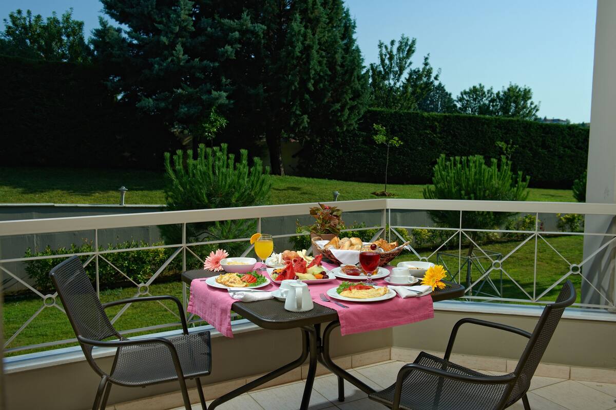 A balcony with a table set for breakfast, including plates of food, a pitcher, and a glass of juice.