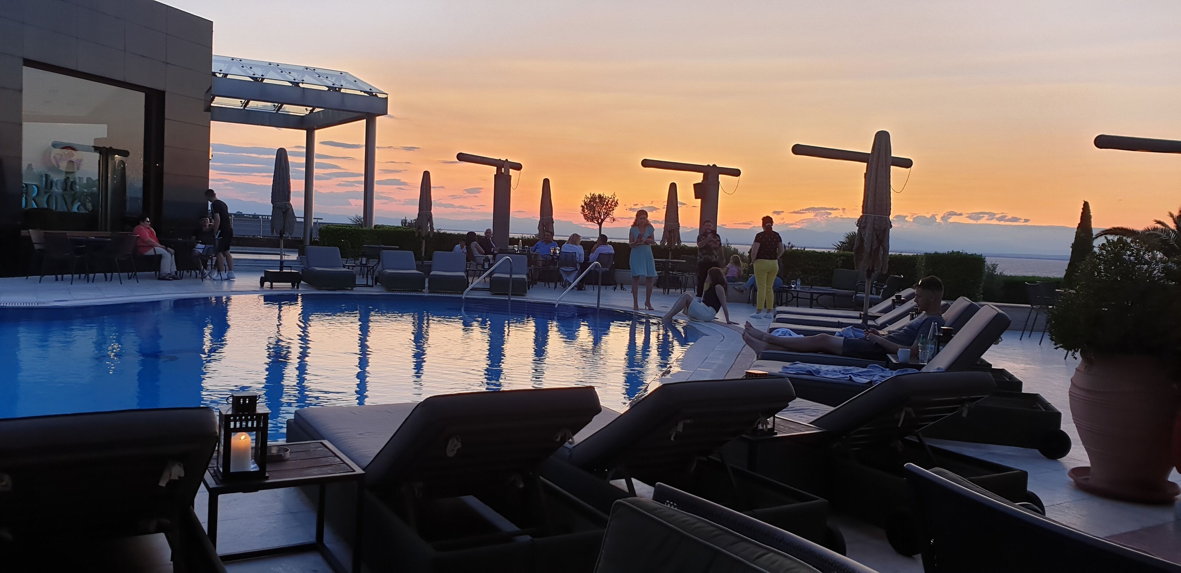 A poolside area with lounge chairs, umbrellas, and a view of the sunset.