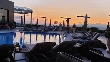 A poolside area with lounge chairs, umbrellas, and a view of the sunset.