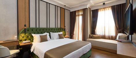 A hotel room with a large bed, a desk, a chair, a TV, and a window with curtains.