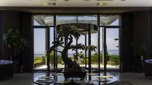 A modern interior with a glass table, a bonsai tree centerpiece, and a view through large glass doors.