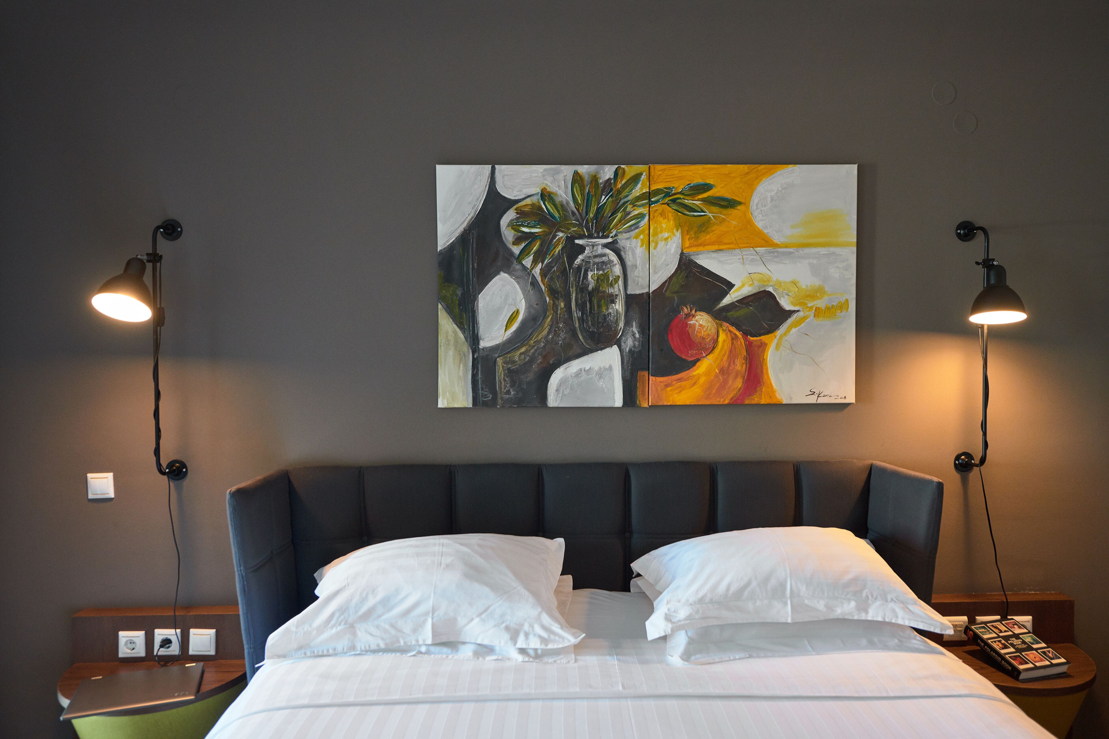 A hotel room with a large bed, two bedside lamps, a nightstand, and a painting on the wall.