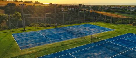 An outdoor tennis court with a net, surrounded by greenery and a view of a distant town.