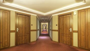 Un couloir d’hôtel avec des portes en bois, un sol recouvert de moquette et un plafond doté d’un éclairage encastré.