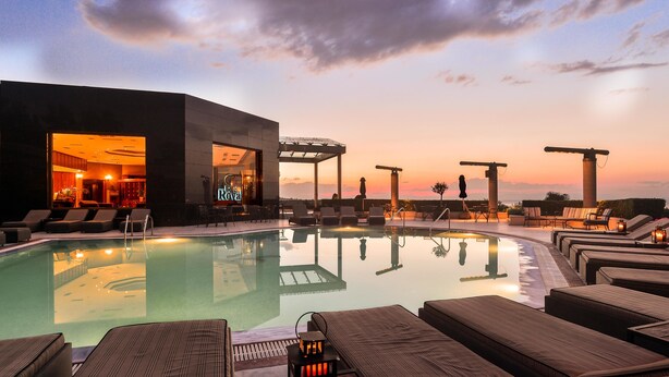 A poolside area with lounge chairs, a bar, and a view of the sunset.