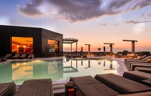 Zona junto a la piscina con sillones de descanso, un bar y vista al atardecer.