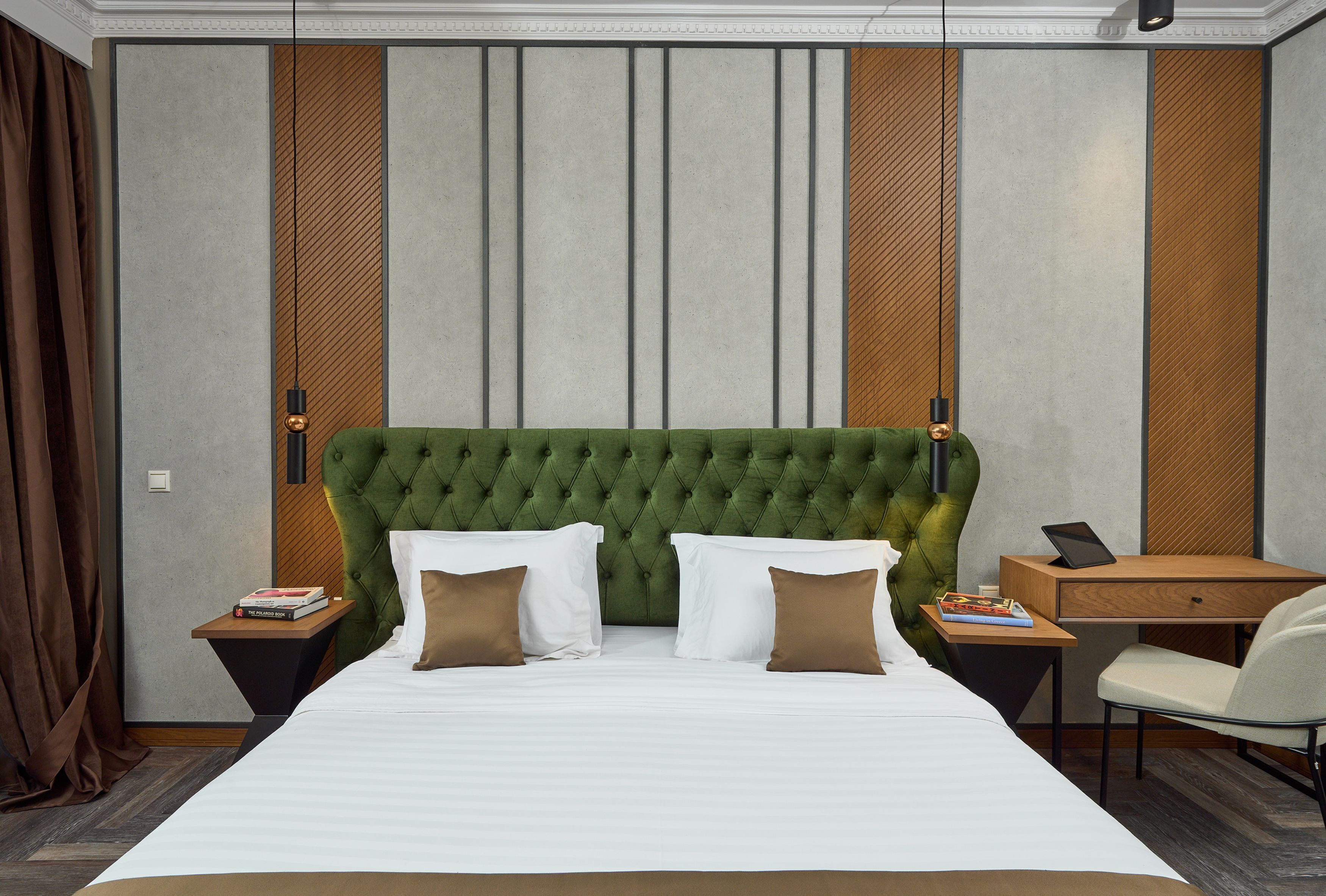 A hotel room with a large bed, a green tufted headboard, two nightstands, a desk, and a chair.