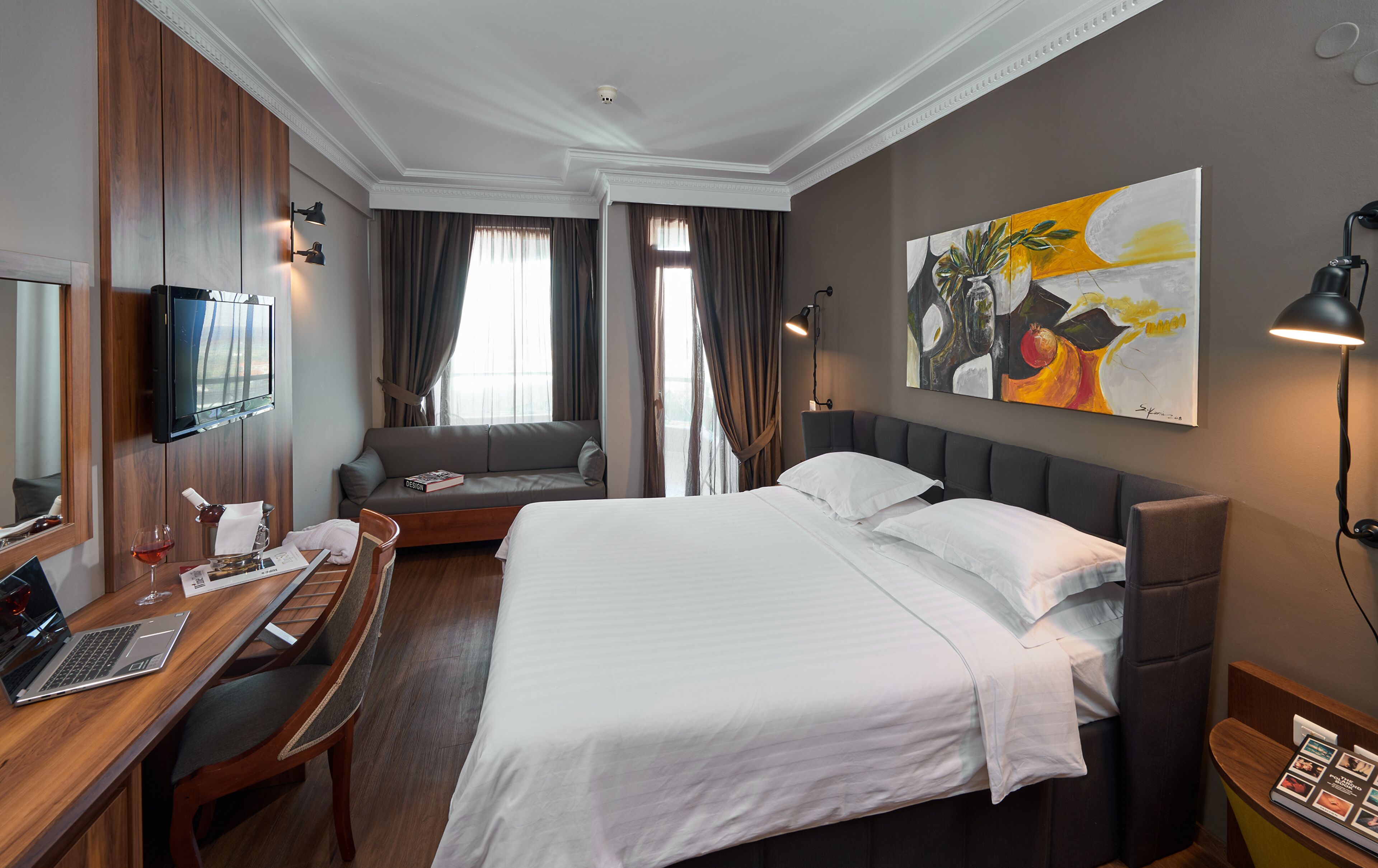 A hotel room with a bed, a desk with a laptop, a sofa, and a TV.