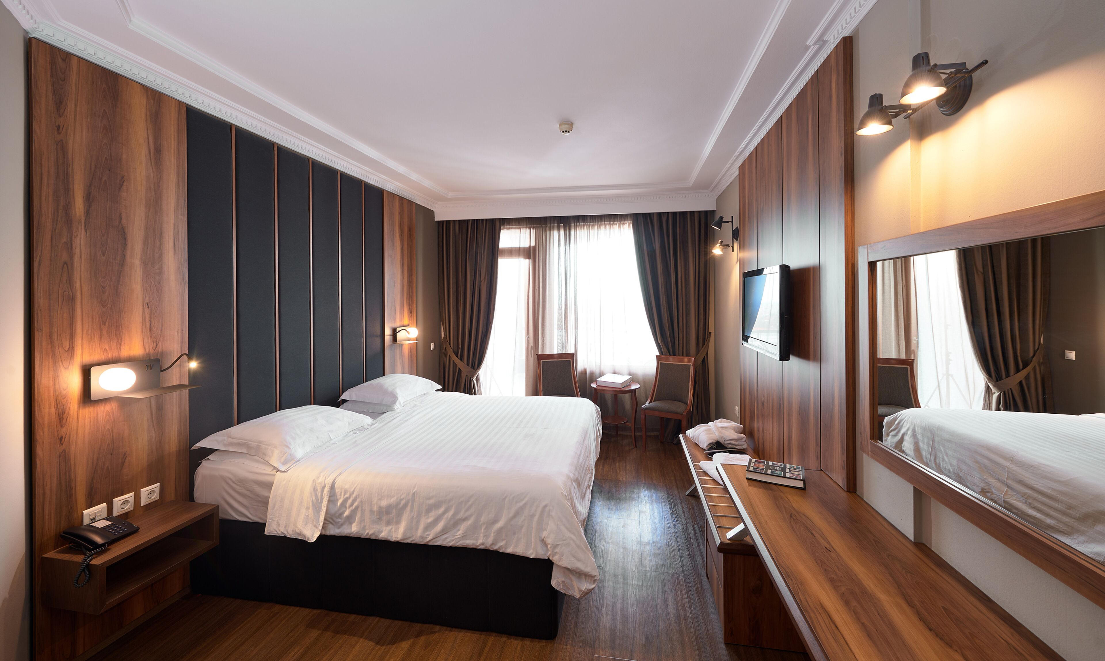 Een hotelkamer met een groot bed, nachtkastjes, een bureau, een stoel, een televisie en een spiegel.