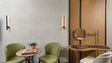 A modern room with two green chairs, a small round table with a magazine, and a wooden side table with a laptop.