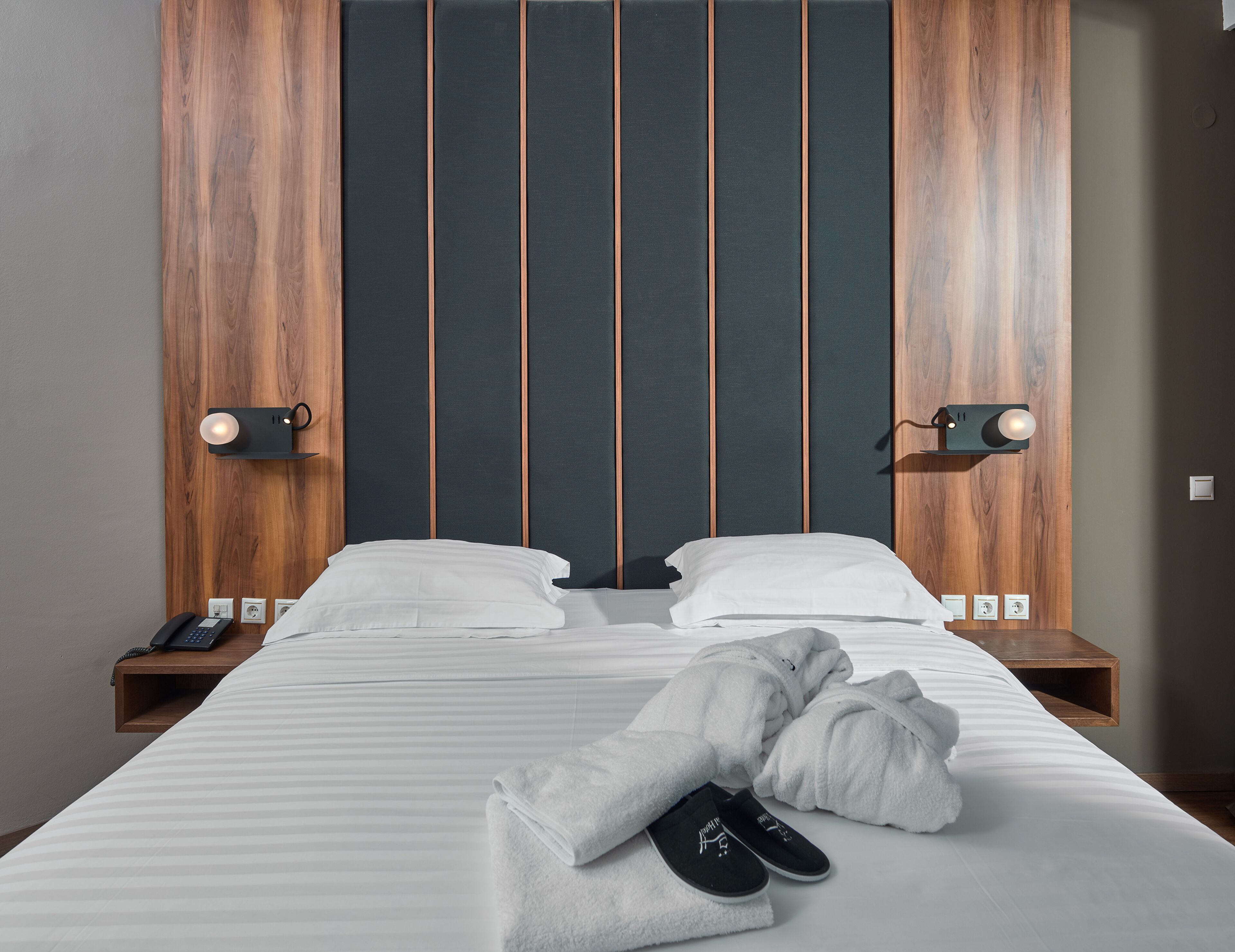 A double bed with a wooden headboard, two bedside tables with lamps, and a pair of slippers on the bed.