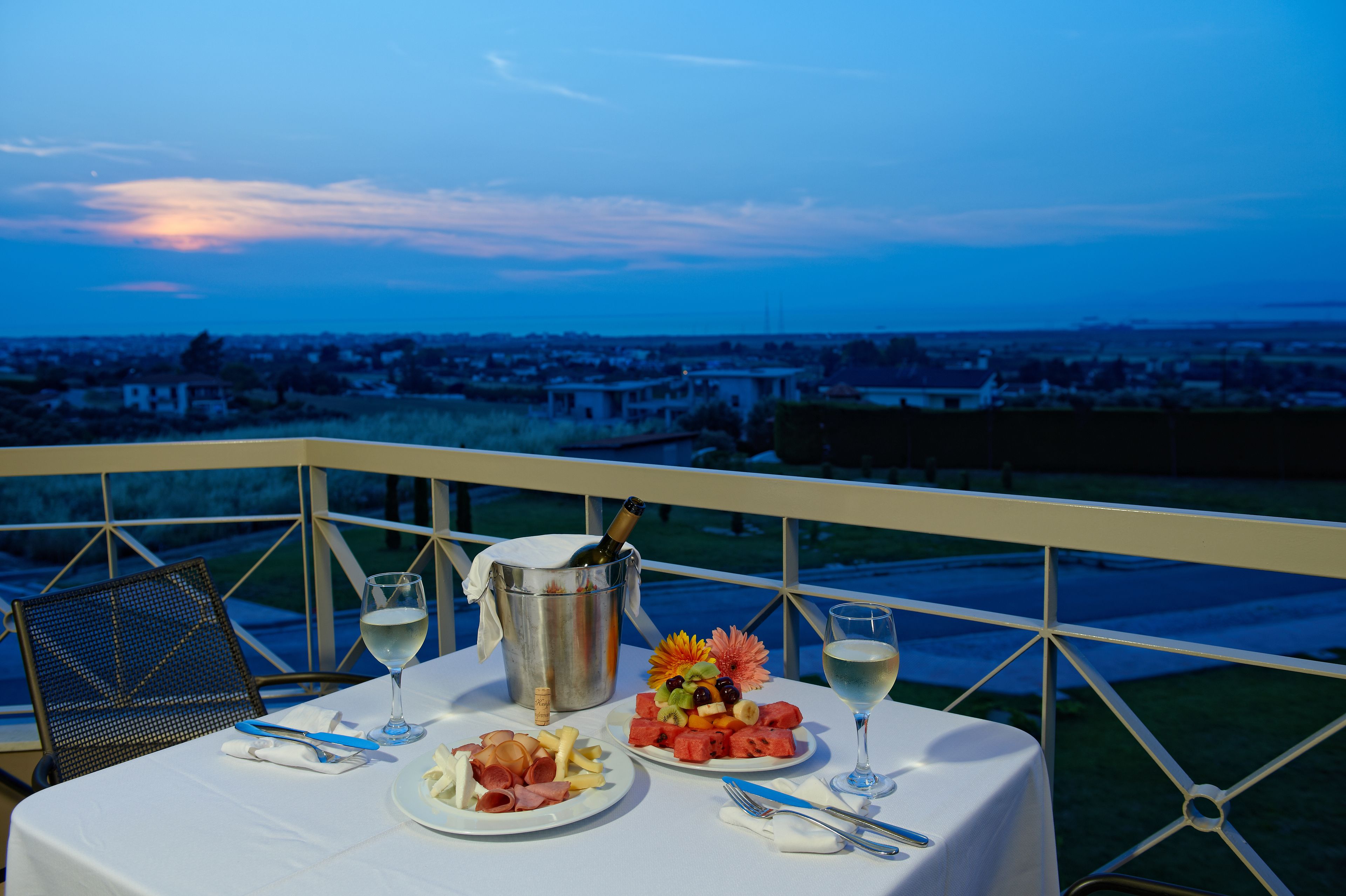 Una mesa con comida y bebidas, con vistas a un paisaje urbano al anochecer.
