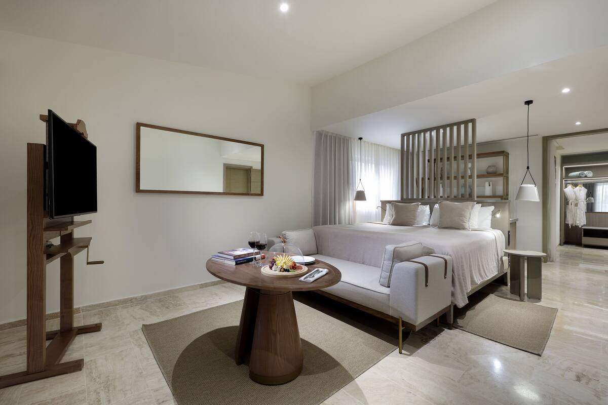 A modern bedroom with a bed, bedside tables, a TV, and a dining area with a table and chairs.