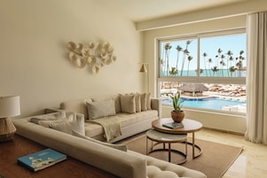 Una sala de estar moderna con un sofá, una mesita de centro y vistas a una piscina y palmeras.