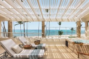 A beachside lounge with a view of the ocean, a hot tub, and lounge chairs.