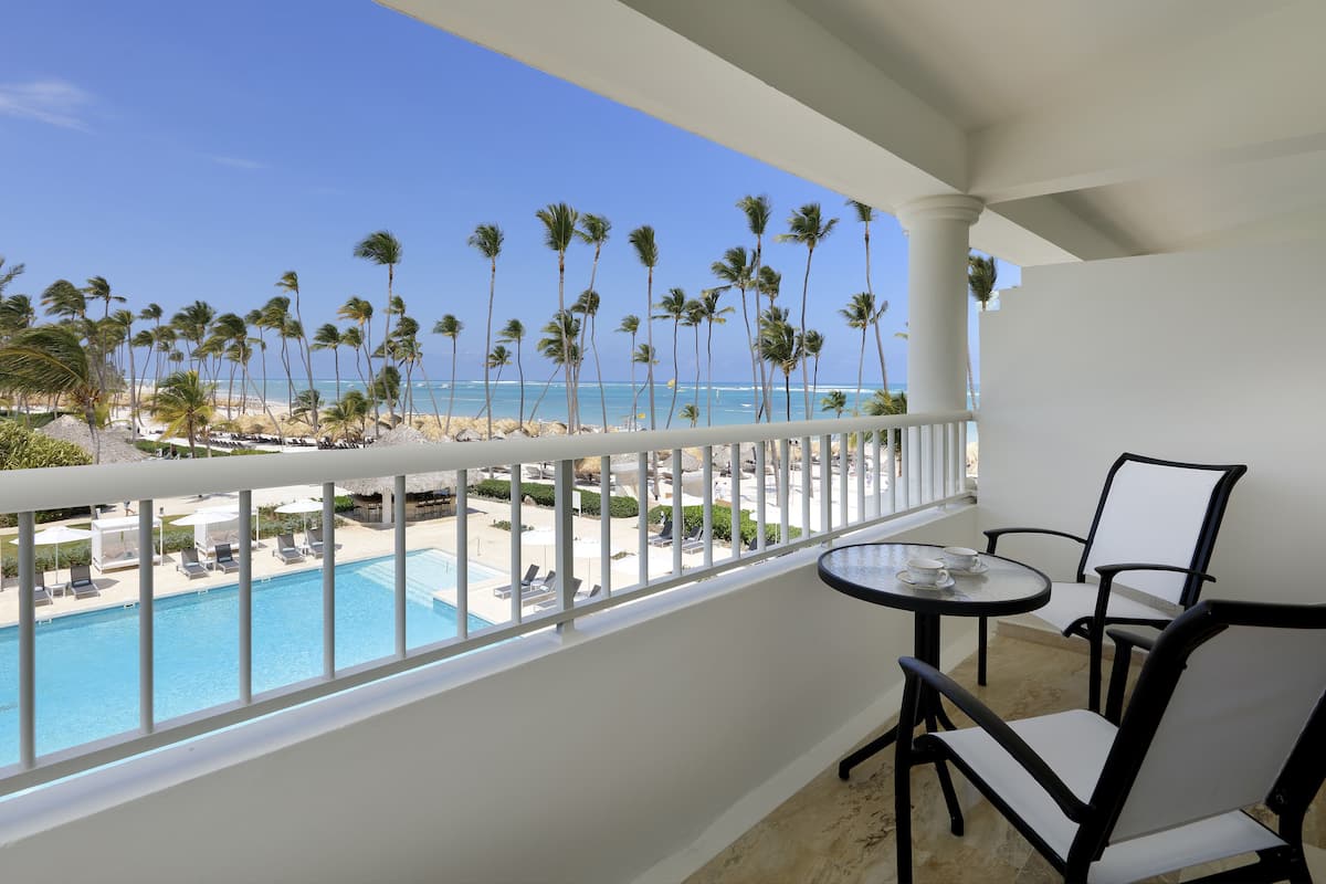 A balcony with a pool view, white chairs, and a table.