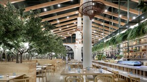 A spacious indoor dining area with wooden tables and chairs, a central column, and a ceiling with wooden beams and hanging lights.