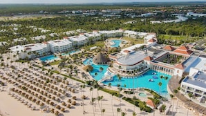 Un resort con diverse piscine, una spiaggia attrezzata con lettini e un edificio imponente con un tetto caratteristico.
