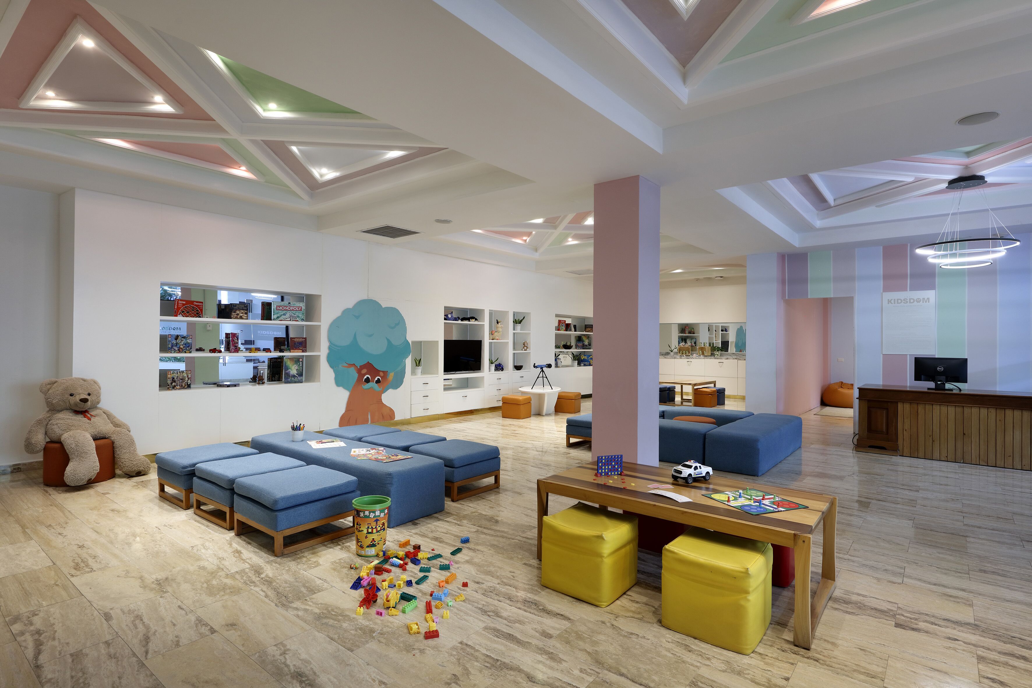 Espaço infantil com área de descanso, brinquedos e um urso de pelúcia grande.