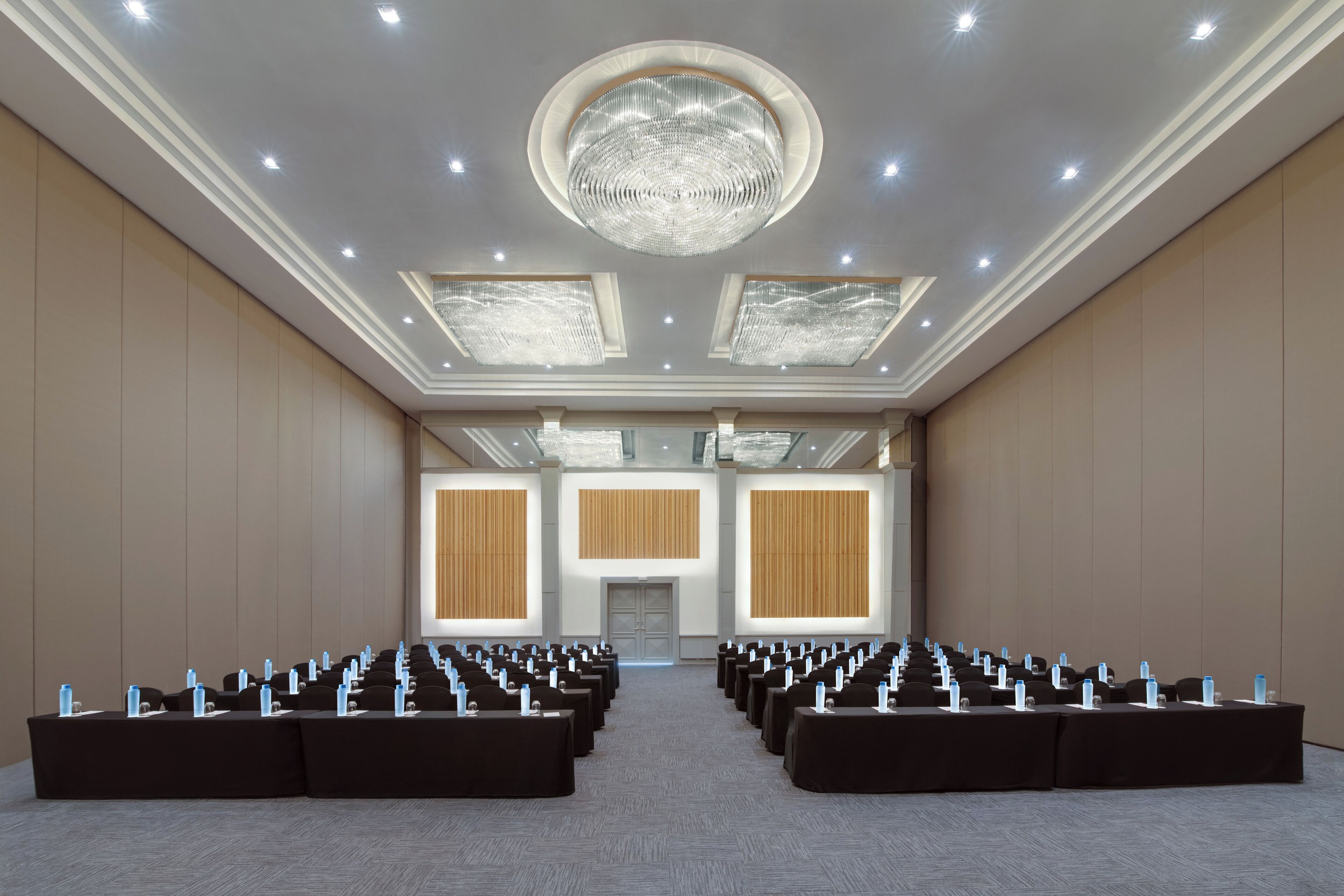 A conference room with rows of tables, a chandelier, and large windows.