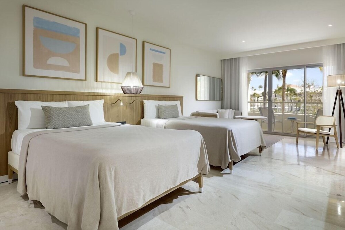A hotel room with two beds, a large window with a view, and artwork on the wall.