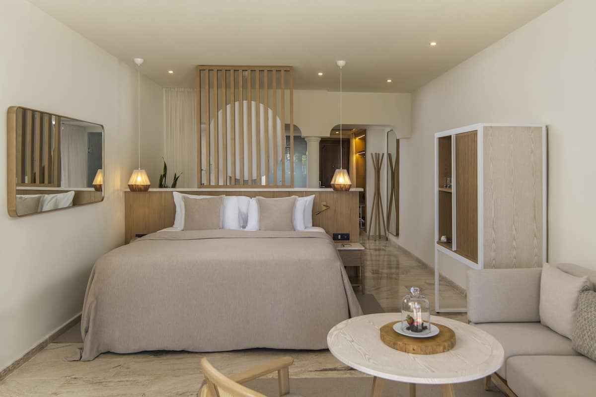 A modern hotel room with a large bed, bedside tables, a round coffee table, and a seating area with a sofa.