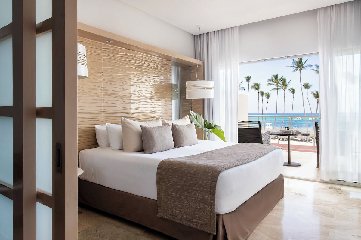 A hotel room with a bed, a view of the beach, and a balcony with a table and chairs.