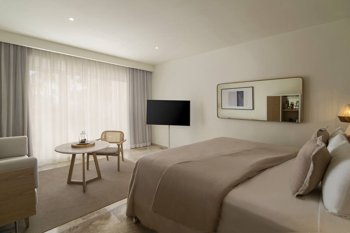 A hotel room with a bed, a TV, a chair, and a small table.