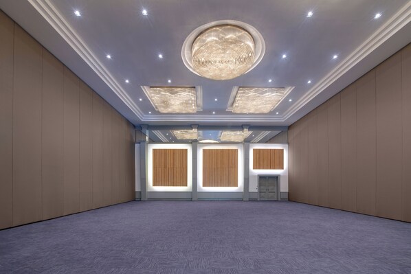 A spacious room with a high ceiling, recessed lighting, and a central chandelier.