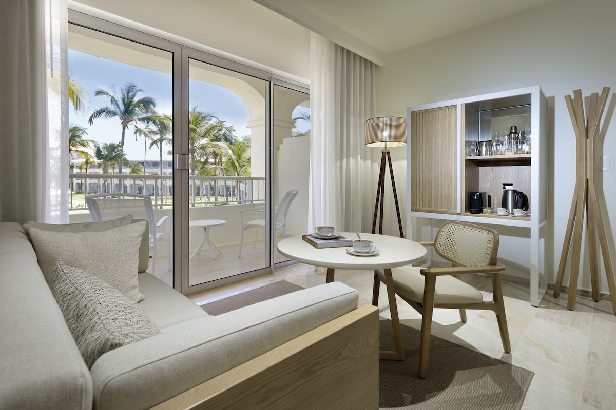 A modern hotel room with a balcony, a sofa, a small table, and a chair.