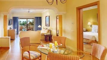 Habitación de hotel con una mesa de vidrio, sillas de mimbre, un sofá, una cama y un balcón con cortinas.