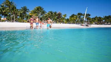 A beach with clear turquoise water, palm trees, and a boat in the background.