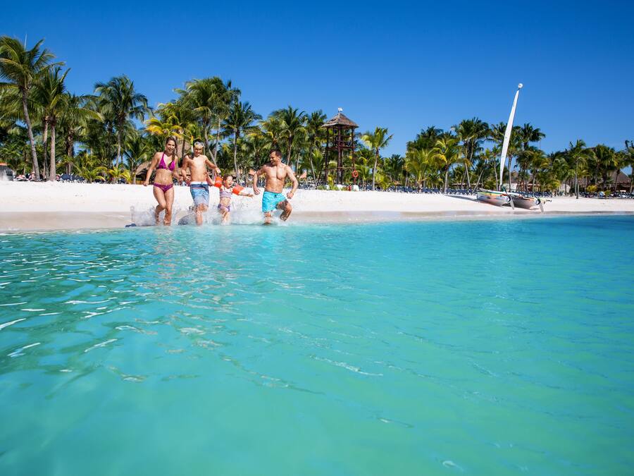 A beach with clear turquoise water, palm trees, and a boat in the background.