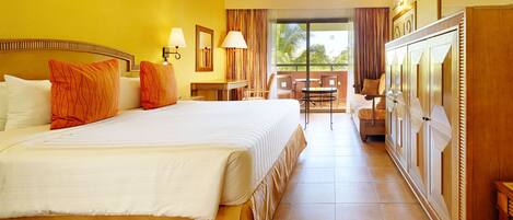 A hotel room with a large bed, a desk, a chair, and a balcony with a view.